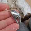 Sterling silver crab claw pendant with silver belcher chain held in hand on natural stone background