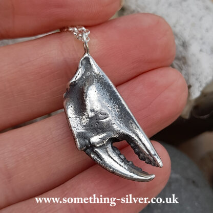 reverse of sterling silver crab claw pendant with silver belcher chain held in hand on natural stone background