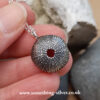 Sterling silver sea urchin shell pendant with silver belcher chain, held in hand on natural stone background