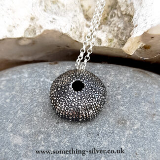 Sterling silver sea urchin shell pendant with silver belcher chain on natural stone background